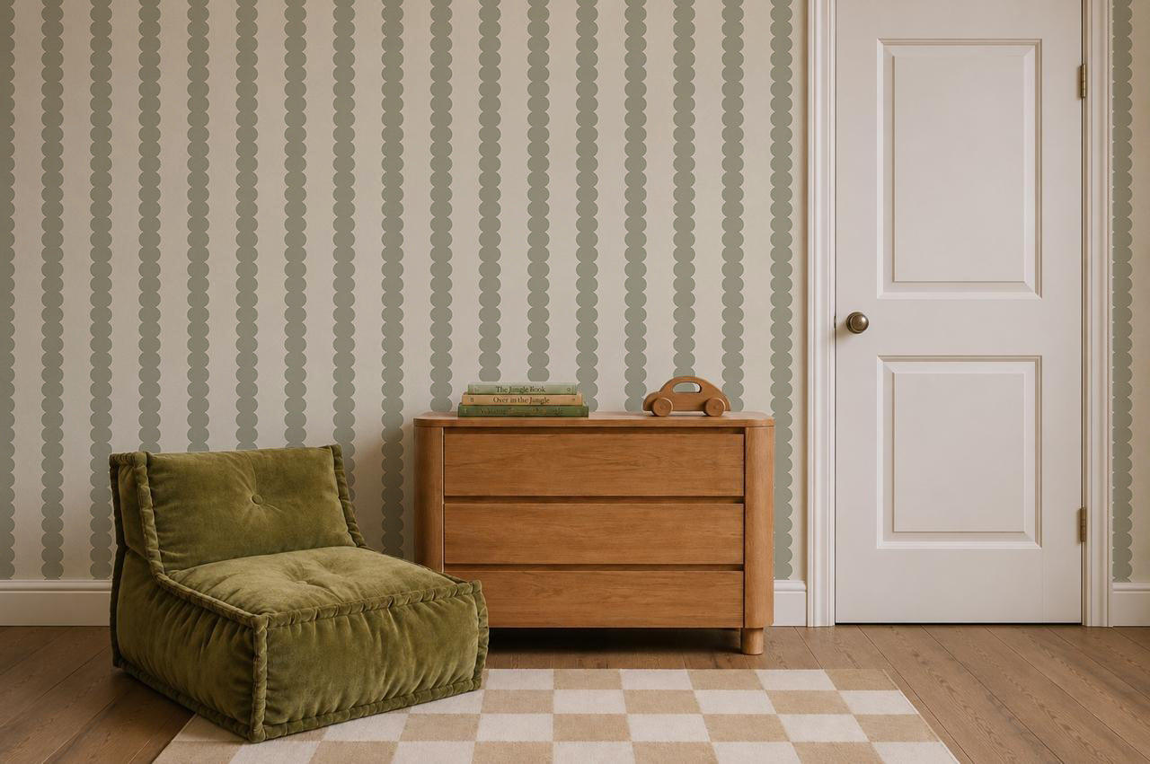 A cozy room featuring a green cushioned chair, wooden dresser, vintage rotary phone, stacked books, a checkered rug, and Scallop Stripe Wallpaper in Green beside a white door on wood flooring.