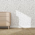 A mid-century wooden dresser stands against a wall finished with Constellation Wallpaper Repeat Pattern, bringing unique style to the space as sunlight creates gentle shadows and a woven rug warms up the modern room.