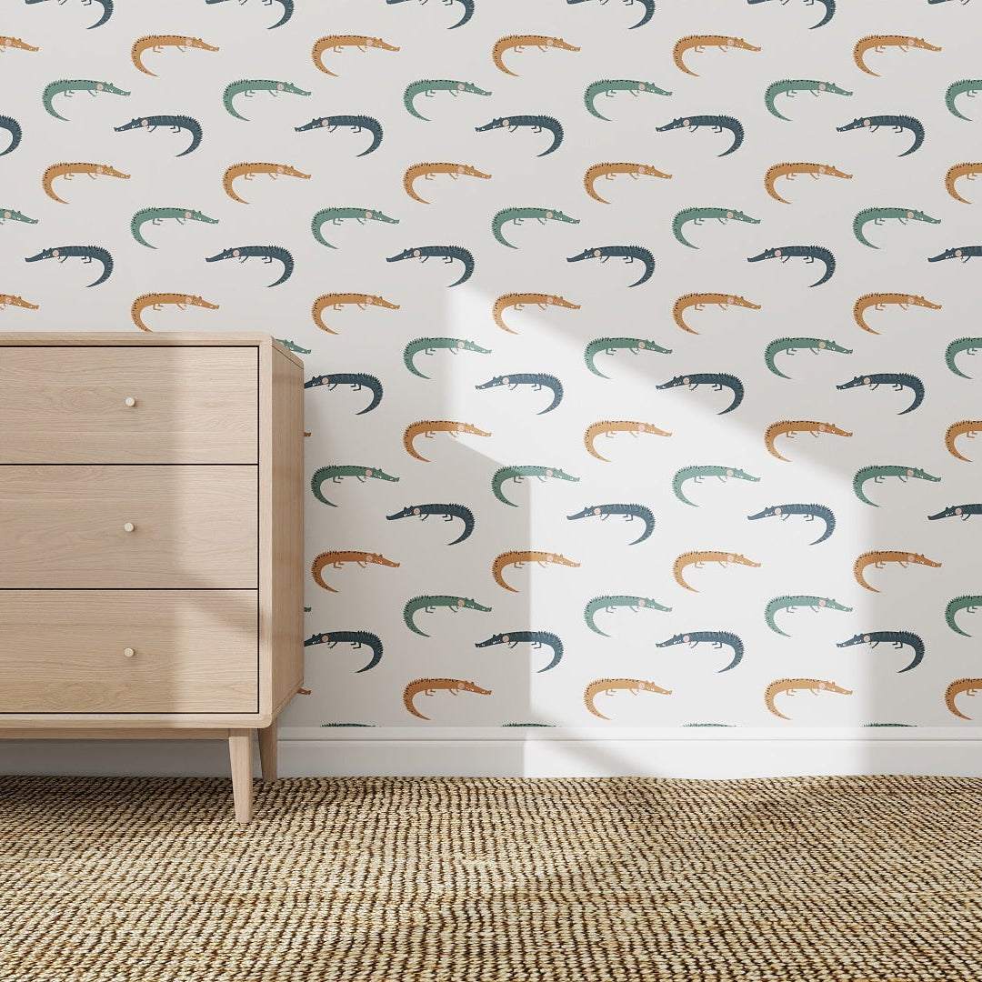 A light wood dresser stands on a woven rug before a white wall covered with Crocodile Wallpaper Repeat Pattern in vibrant colors, creating a playful look as sunlight casts soft shadows across the scene.