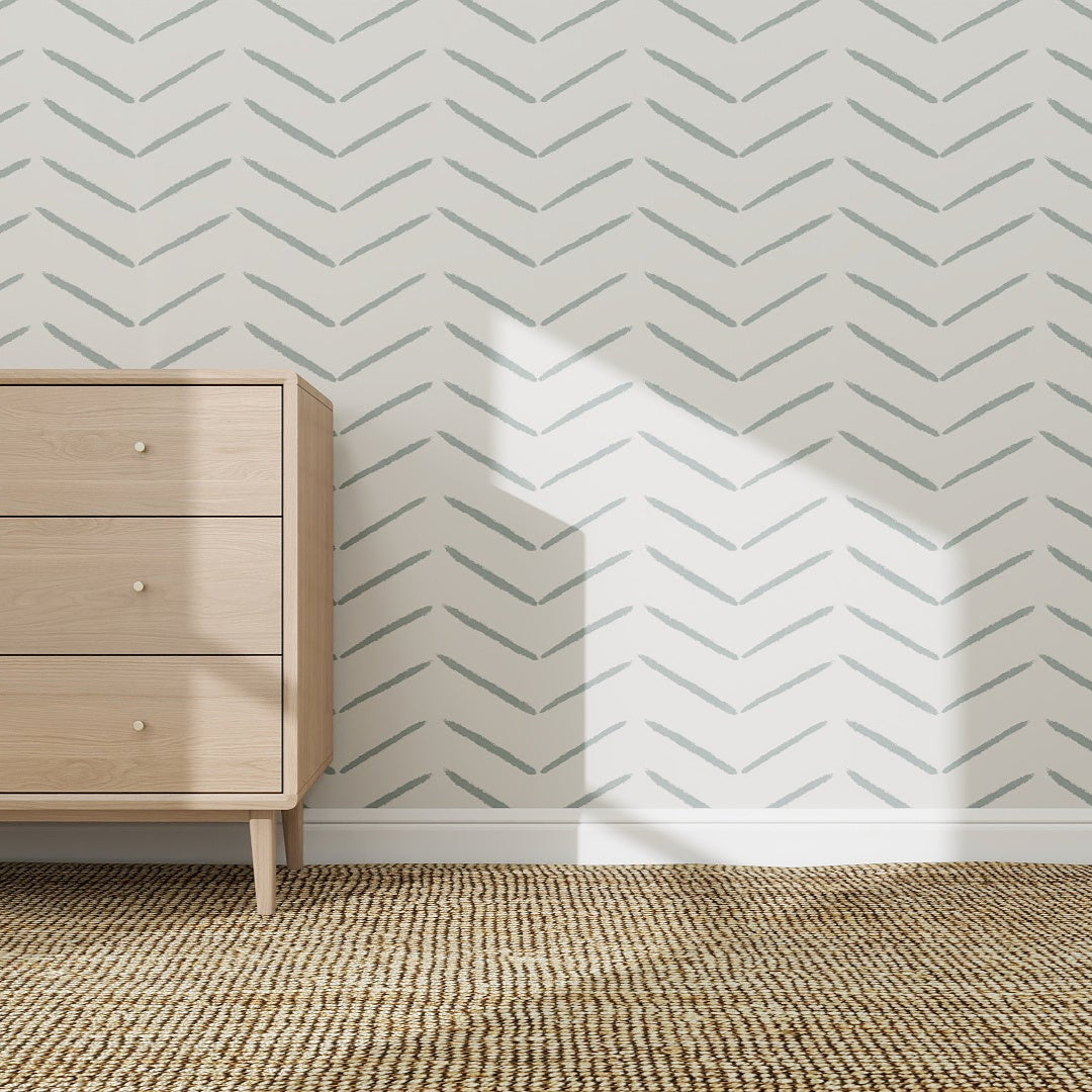 A light wood dresser sits on a woven tan carpet against a wall covered with Herringbone Wallpaper Repeat Pattern | Blue, adding a modern touch. Sunlight casts shadows, creating a bright and airy atmosphere.