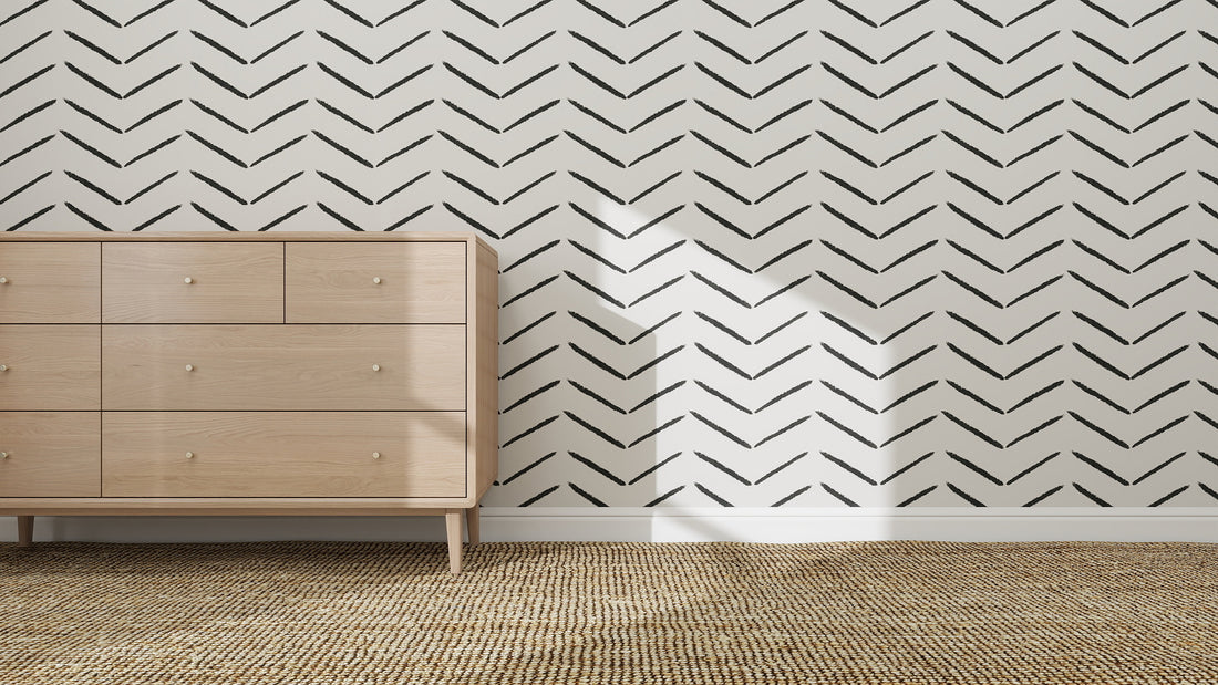 A light wood dresser with six drawers is set on a woven rug against a white wall adorned with Herringbone Wallpaper Repeat Pattern in Charcoal, as sunlight casts window shadows, enhancing the space’s elegant interior design.