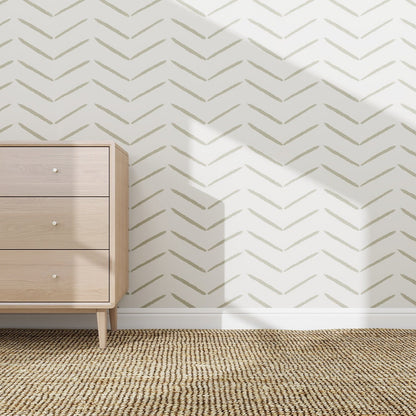 A light wooden dresser stands on a woven rug beside a white wall decorated with Herringbone Wallpaper Repeat Pattern | Olive. Sunlight casts sharp shadows, adding a stylish touch to the serene setting.