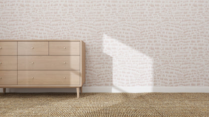 A light wood dresser with multiple drawers stands on a woven rug beside the Daphne Drops Wallpaper Repeat Pattern in pink, sunlight casting bright shadows and enhancing the whimsical feel of the room.