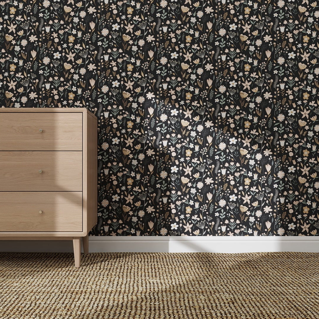 A light wood dresser sits on a tan rug before an elegant charcoal wall adorned with the Millie Floral Wallpaper Repeat Pattern | Charcoal, as sunlight casts gentle shadows across the floor and striking wallpaper update.