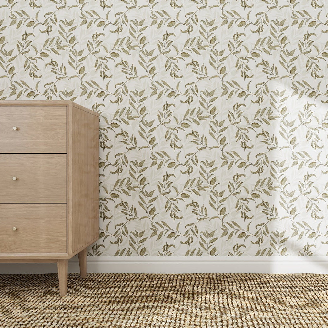 A light wood dresser with three drawers stands on a woven beige rug, set against a wall adorned with Dreamy Vines Wallpaper Repeat Pattern in soft green and white, its leafy design highlighted by sunlight’s gentle shadow.