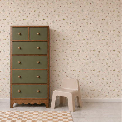 A green and wood dresser stands next to a small beige plastic chair on a checkered rug, set against a cream wall adorned with Elsies Verdant Garden Wallpaper.