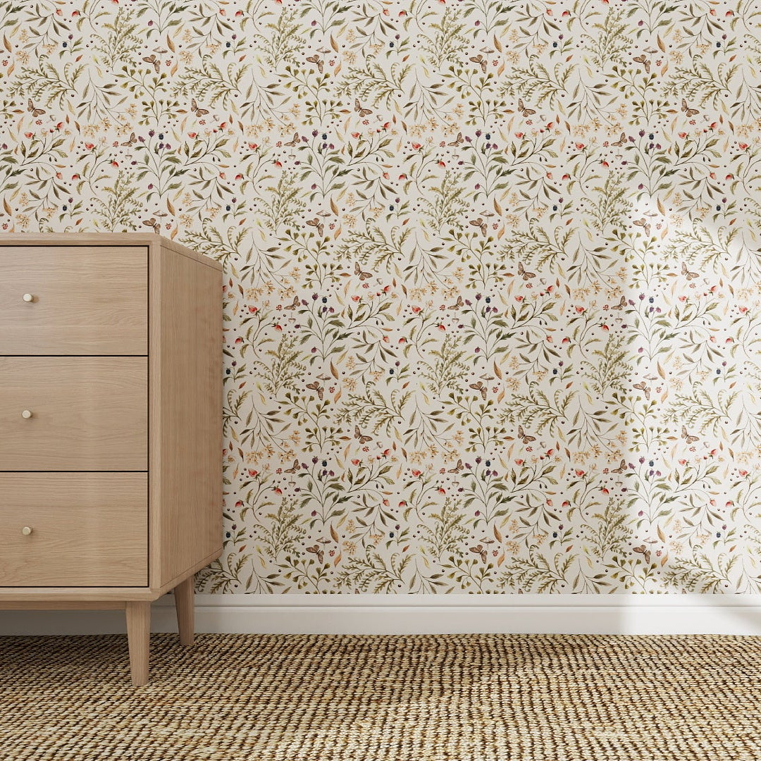 A light wood dresser with three drawers sits on a woven rug beside a wall covered in Forest Floor Wallpaper Repeat Pattern, featuring leaves and small flowers in soft, earthy tones.