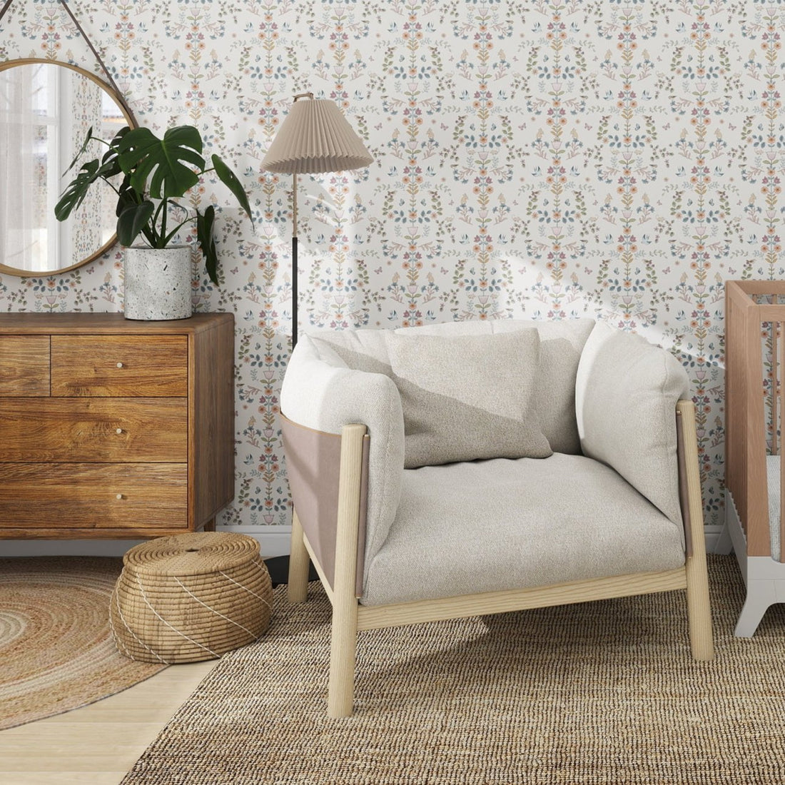 A cozy living room showcases a beige armchair, rattan side table, wooden dresser with a round mirror and potted plant. The wall adorns munks and mes Forest Tales Wallpaper Repeat Pattern, while a woven rug adds texture to the floor. A tall lamp stands beside the chair.