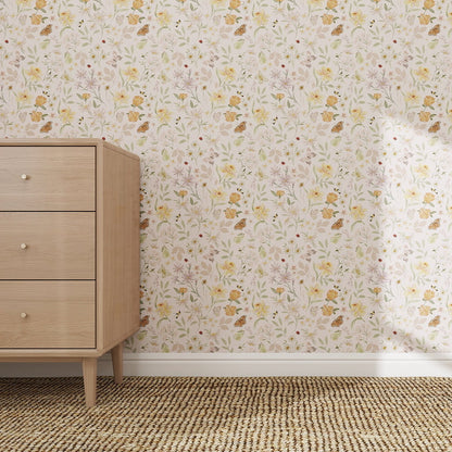 A wooden dresser with three drawers stands on a woven rug beside a wall featuring the Garden Symphony Wallpaper Repeat Pattern | Sample in soft pastel florals. The scene is brightly lit and minimalist.