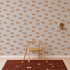 A wooden chair sits on a patterned rug in front of a wall adorned with Goldies Cheetah Wallpaper in Blue, featuring playful cheetahs and repeating orange leopard prints. A gold wall sconce is mounted to the right of the chair.