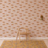 A wooden chair sits on a patterned rug in front of Goldies Cheetah Wallpaper in Pink, featuring a lively pattern of repeating orange cheetahs for a playful touch. A gold wall sconce is mounted to the right of the chair.