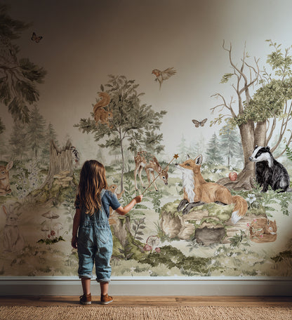A young girl in overalls stands on a wooden floor, reaching out to touch the Into The Forest Wallpaper Mural, which features a hand-painted woodland scene with animals such as a fox, badger, deer, birds, and trees.