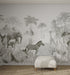 The Custom Jungle Mural Wallpaper V1_2 | Sample features a grayscale scene of African animals among palm trees and foliage, with a white cushioned bench placed on a woven rug in a modern, minimalist room.
