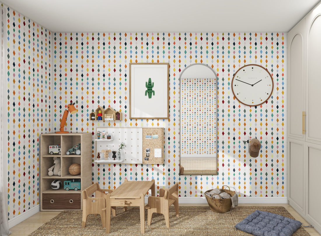 A vibrant kids room features Jolly Jester Wallpaper Repeat Multi by munks and me with raindrop designs. The wooden furniture includes a small table, chairs, a toy-filled cabinet, and a wicker basket. A clock and mirror decorate the wall while the floor is graced with a colorful woven rug.