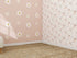 A corner room with tan woven carpet features one wall in Custom Large Daisy Floral Wallpaper Repeat Pattern—white and yellow daisies on pink—while sunlight adds gentle shadows across the space.