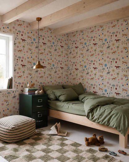 A cozy bedroom with green bedding on a wooden bed, a checkered rug, toys, books, and nursery walls decorated with Little Wanderers Wallpaper featuring colorful animals. Sunlight pours in through the window.