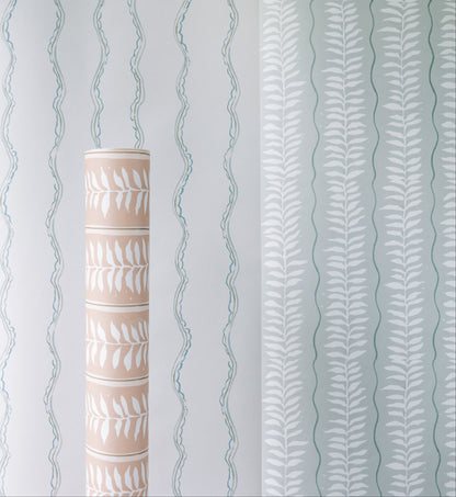 A roll of Meadow Leaf Stripe Wallpaper in Sea Foam with a beige background and white leaf pattern is placed upright against a wall displaying vertical leafy and wavy designs in light blue and white.