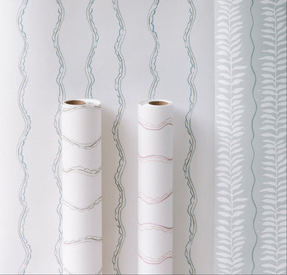 Two rolls of Ribbon Stripe Wallpaper, Blue, with wavy pastel patterns are displayed in front of a wall featuring blue wavy lines and white leafy designs on light blue—ideal for elegant children’s room decor.