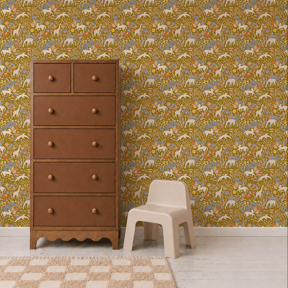 A brown wooden dresser and a small beige plastic chair sit on a light floor beside a tan-checkered rug, while the Mils Menagerie Wallpaper, Gold showcases deer and trees in vibrant yellow, green, and orange tones, bringing a playful touch of nature to the space.