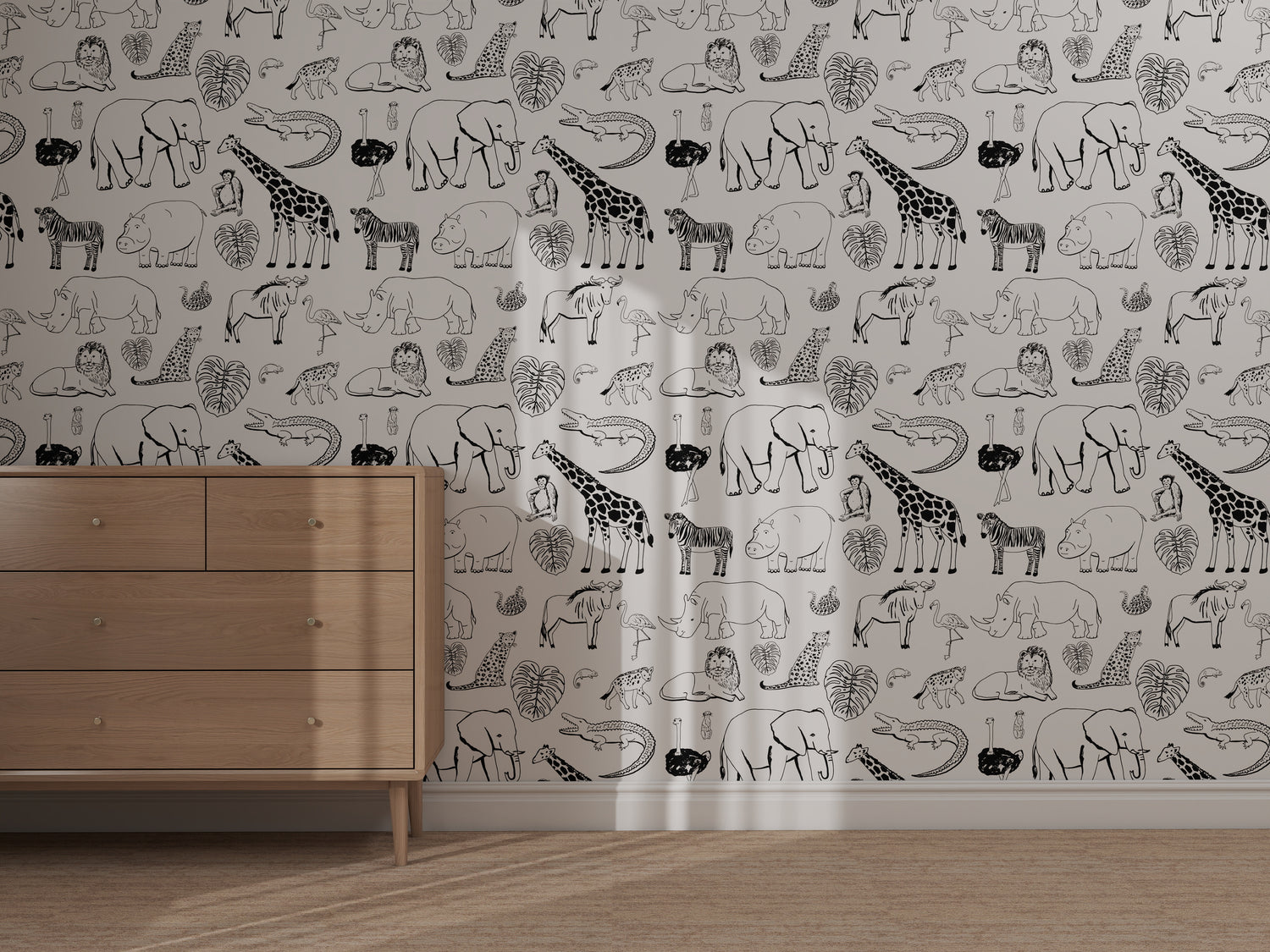 A light wooden dresser stands before the Going on Safari Wallpaper Repeat Pattern | Black and White, showcasing black-and-white giraffes, rhinos, elephants, leopards, and leaves as sunlight casts soft shadows on the illustrations.