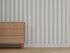A wooden dresser with six drawers stands on a beige carpet beside a wall covered in Custom Blue Scallop Stripe Wallpaper.