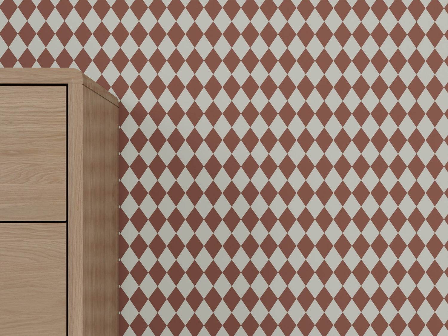 A light wood dresser stands against a wall covered in Diamond Dancer Wallpaper, Stone Rose, showcasing an artisanal pattern of red and white harlequin diamonds.