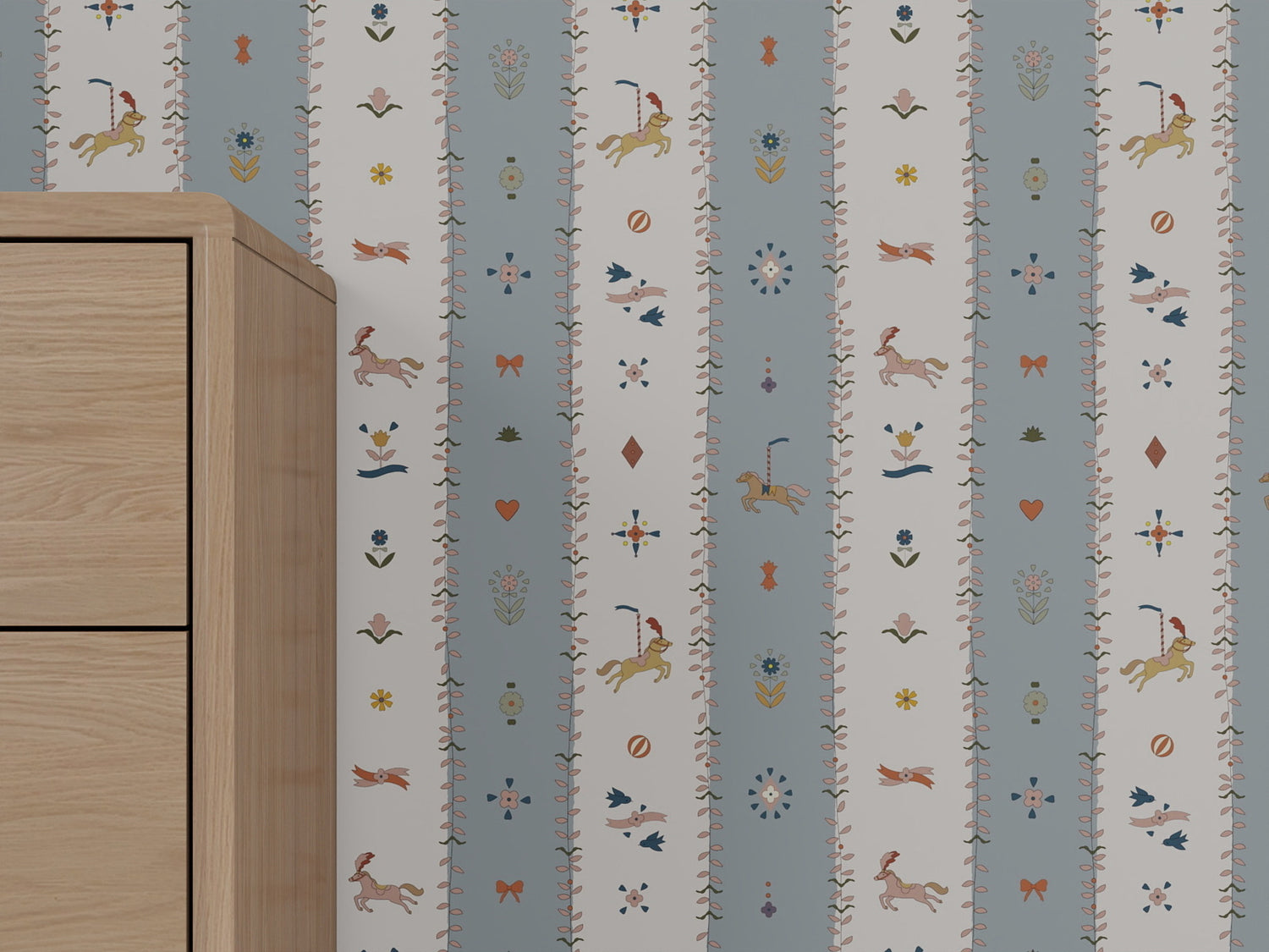A light wooden cabinet stands beside a wall covered in The Little Carousel Stripe Wallpaper, Blue, which features blue and white stripes with whimsical animals, floral motifs, hearts, and charming decorative details.