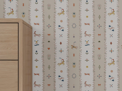A section of The Little Carousel Stripe Wallpaper, Rose, with vertical stripes in light hues and whimsical unicorns, birds, flowers, hearts, and other motifs; a light wooden cabinet appears partially on the left.