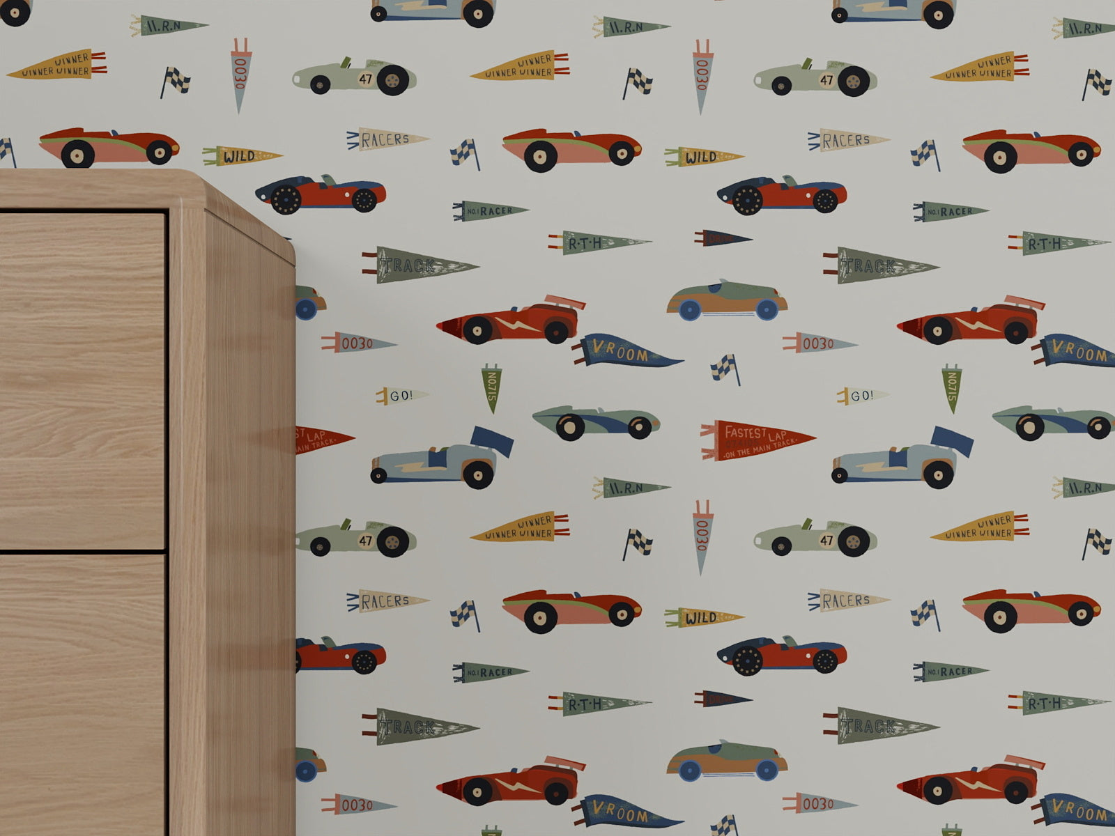 A light-colored wall is decorated with Speedway Dash Wallpaper, showcasing a playful pattern of vintage race cars, checkered flags, and colorful pennants—ideal nursery decor. A wooden cabinet appears partially on the left side of the image.