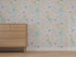 A light wooden dresser with four drawers stands on a beige carpet, backed by Custom Wildflower Waltz Wallpaper | Sample, which features colorful pastel flowers and green leaves in a high-quality floral pattern.