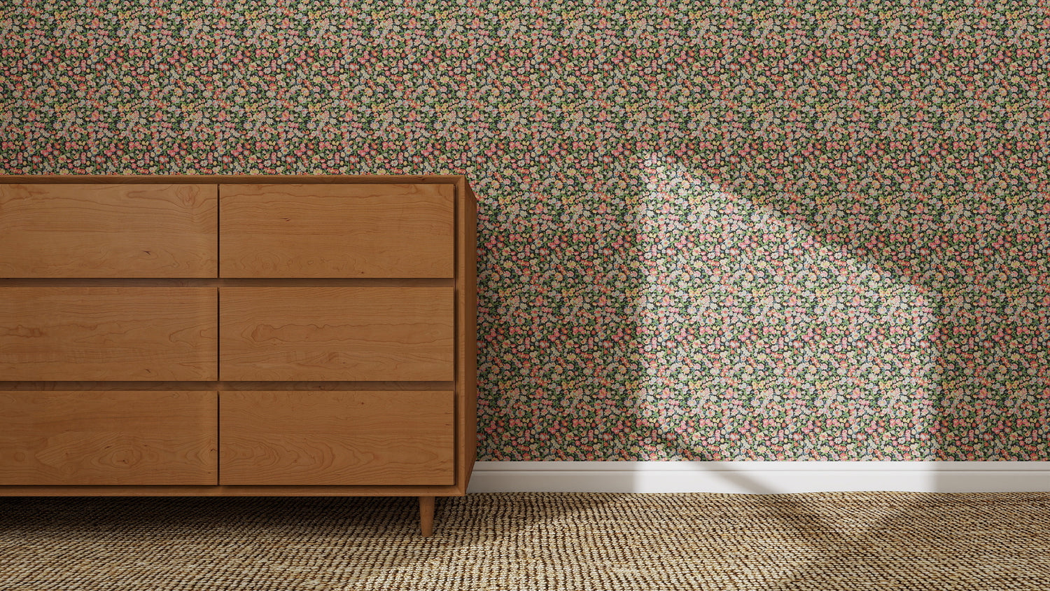 A wooden dresser stands by a wall covered in Midnight Meadow Florals Wallpaper | Sample, highlighting its vibrant colors. Sunlight casts an angular shadow across the wallpaper, while a woven carpet lies on the floor.