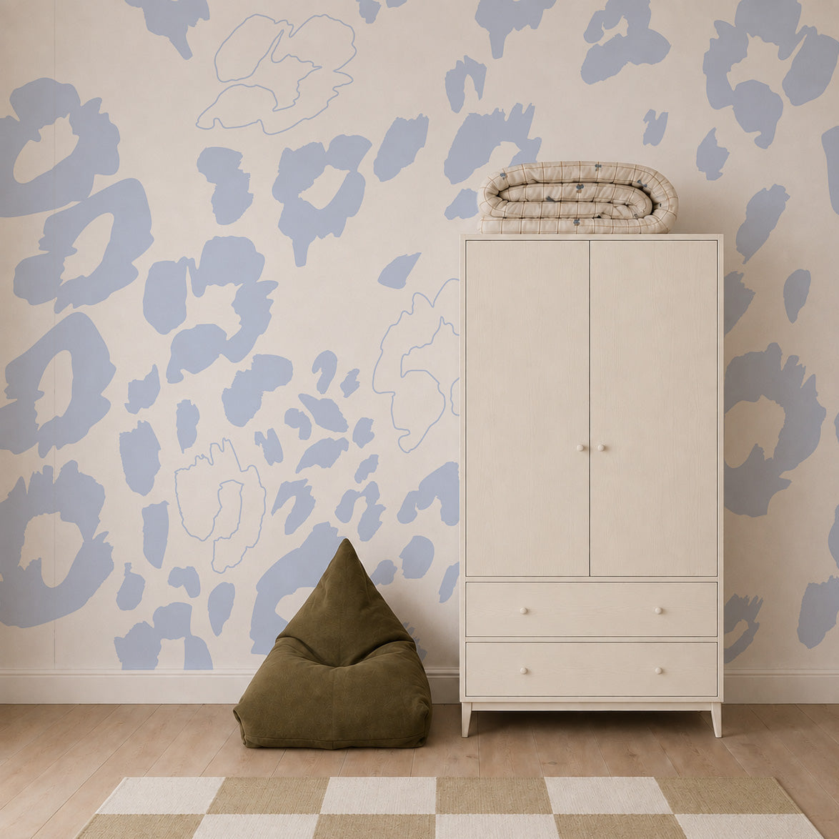 A minimalist room featuring the Nelly Leopard Print Mural as kids room wallpaper, a white wardrobe with blankets on top, a green bean bag chair, and a beige checkered rug on a wooden floor.
