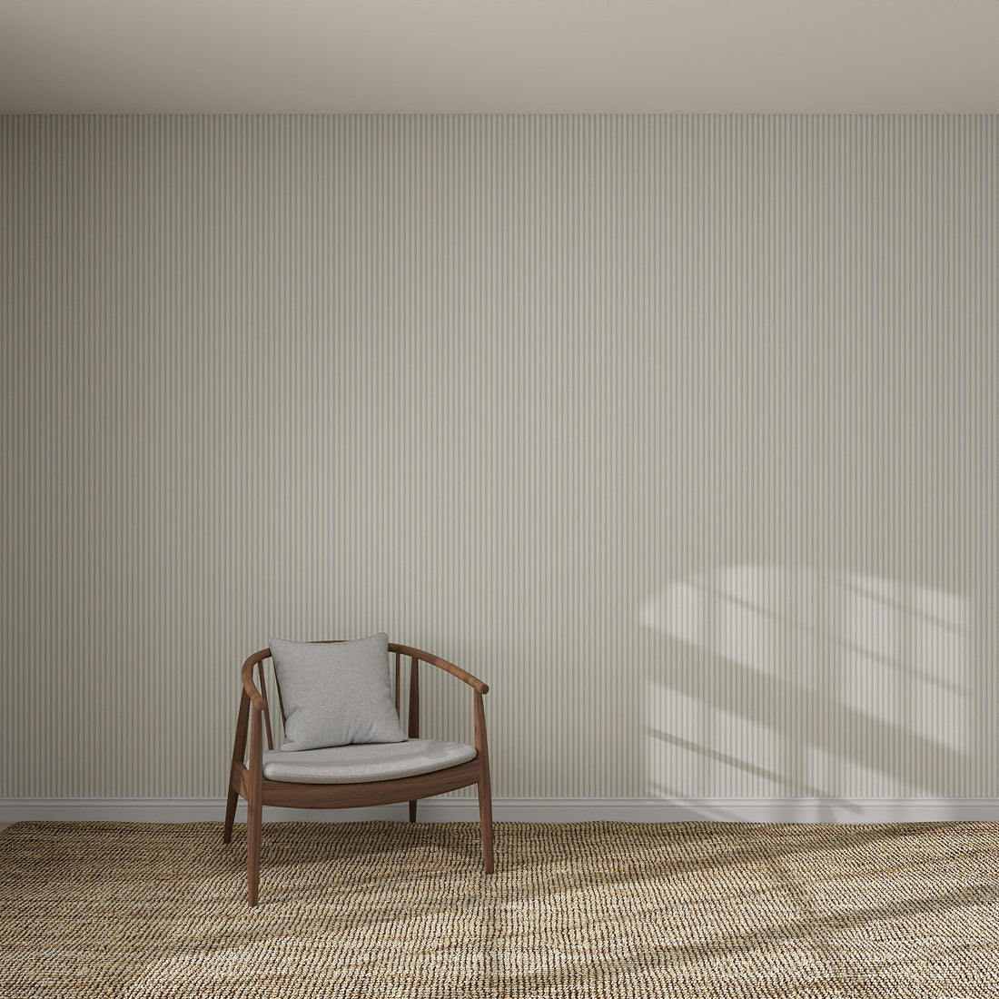 A wooden armchair with a gray cushion sits on a woven rug before Pico Stripe Wallpaper Blue | Sample, its light vertical stripes elegantly displayed as sunlight casts shadows on the wall and floor.