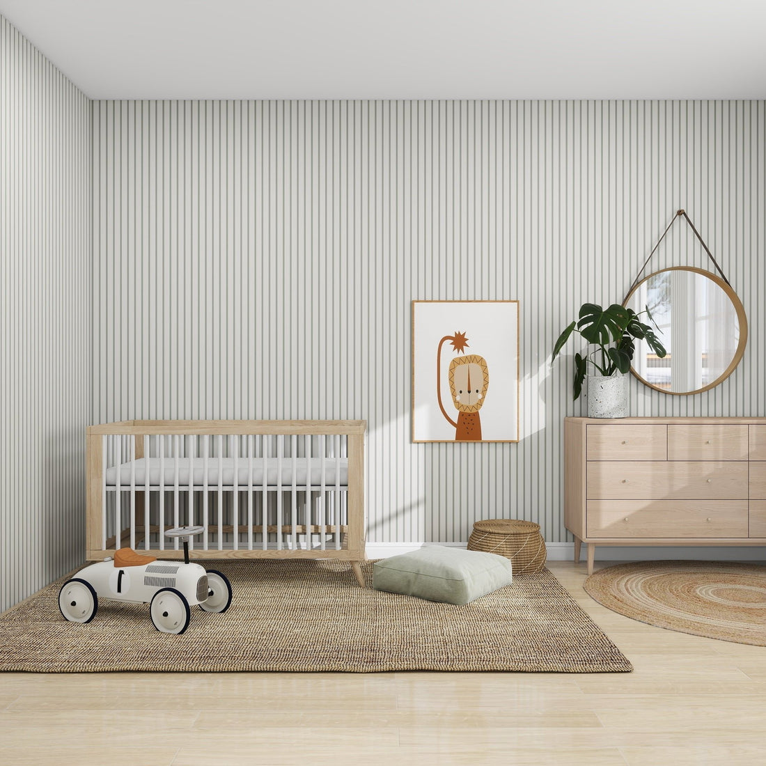 A modern nursery features a wooden crib, a white toy car on a woven rug, and a light wood dresser with a round mirror and plant. A framed lion print enhances the walls color quality with munks and me Pinstripe Wallpaper Matcha. A soft cushion rests on the floor, completing the serene setting.