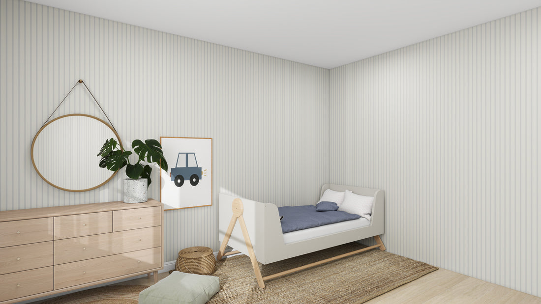 In a minimalist nursery, a small bed with blue bedding is paired with a wooden dresser and round mirror. A potted plant and framed car picture accent the walls adorned in munks and mes Pinstripe Wallpaper Sky, complemented by a woven rug on the wooden floor.