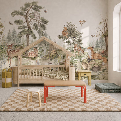 Children’s bedroom featuring the “Into The Forest Mural” with charming forest animals, a cozy house-shaped wooden bed, small table with red legs, green floor cushion, two storage baskets, and a checkered beige rug.