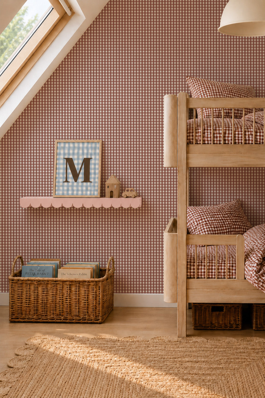 A wooden bunk bed sits next to a pink scalloped shelf holding a framed letter M and small wooden toys, with a woven basket of children’s books on the floor in front of Mini Check Wallpaper Sample, Red.