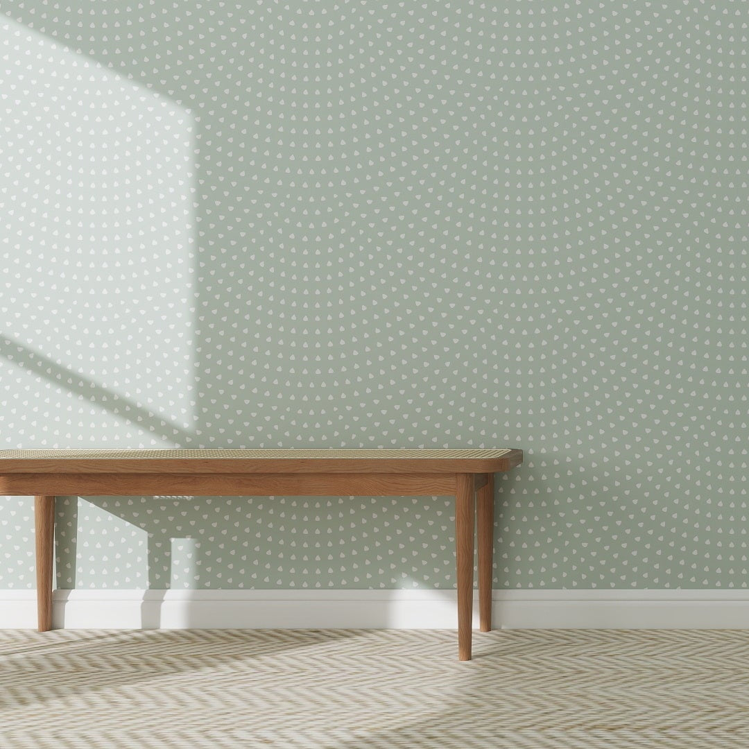 A wooden bench is placed on a patterned rug before a green wall decorated with Scallop Shell Wallpaper in Turquoise, sunlight streaming in from the left.