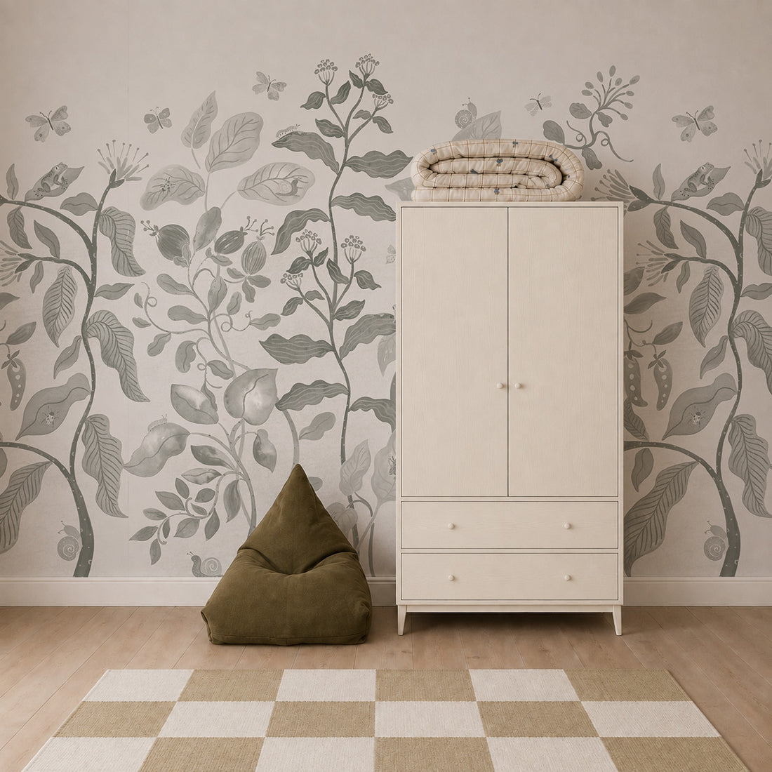 A room with the Secret Garden Mural in Sage featuring leafy patterns, a beige wardrobe with folded quilts on top, a green bean bag chair, and a beige and white checkered rug on a wooden floor.