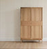 A light wooden cabinet with four panels stands on a wooden floor against a wall adorned with All I See Is Magic Stripe Wallpaper, featuring vertical lines of small colored dots.