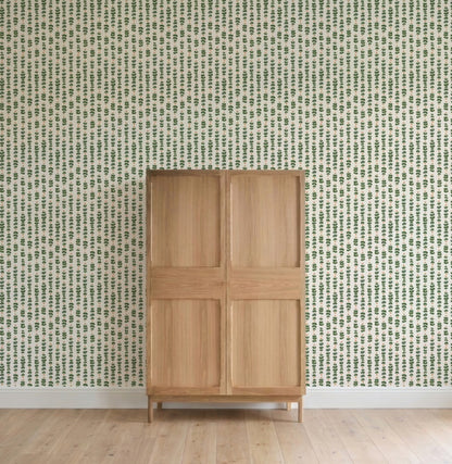 A light wooden cabinet stands on a light wood floor against a wall covered with Floral Trails Wallpaper featuring a small green leaf pattern in rows.