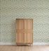 A light wooden cabinet stands on a light wood floor against a wall covered with Floral Trails Wallpaper featuring a small green leaf pattern in rows.
