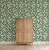 A wooden cabinet with a modern four-panel design stands on a light wood floor against a wall covered in How Lucky We Are Clovers Wallpaper.
