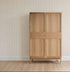 A simple wooden wardrobe with four panel doors stands against a wall adorned with Jacquard Stars Wallpaper in gold. Light wood flooring and white baseboards complete the room&