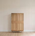 A simple wooden cabinet with four panels stands against a wall adorned with Jacquard Stars Wallpaper, Red, in a room featuring light wood flooring.