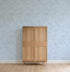 A simple wooden cabinet with four panels stands against a light wood floor and a wall decorated with Painted Cloud Stars Wallpaper, Blue, featuring subtle white speckles for a celestial effect.