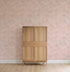 A wooden wardrobe with four panels stands against a pink wall adorned with Painted Cloud Stars Wallpaper, Rose. The light wood floor and minimal decor create an uncluttered, serene nursery setting.