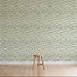 A simple wooden stool sits on a light wood floor in front of a wall adorned with Floral Trails Wallpaper, displaying vertical rows of small green leafy plants on a crisp white background.