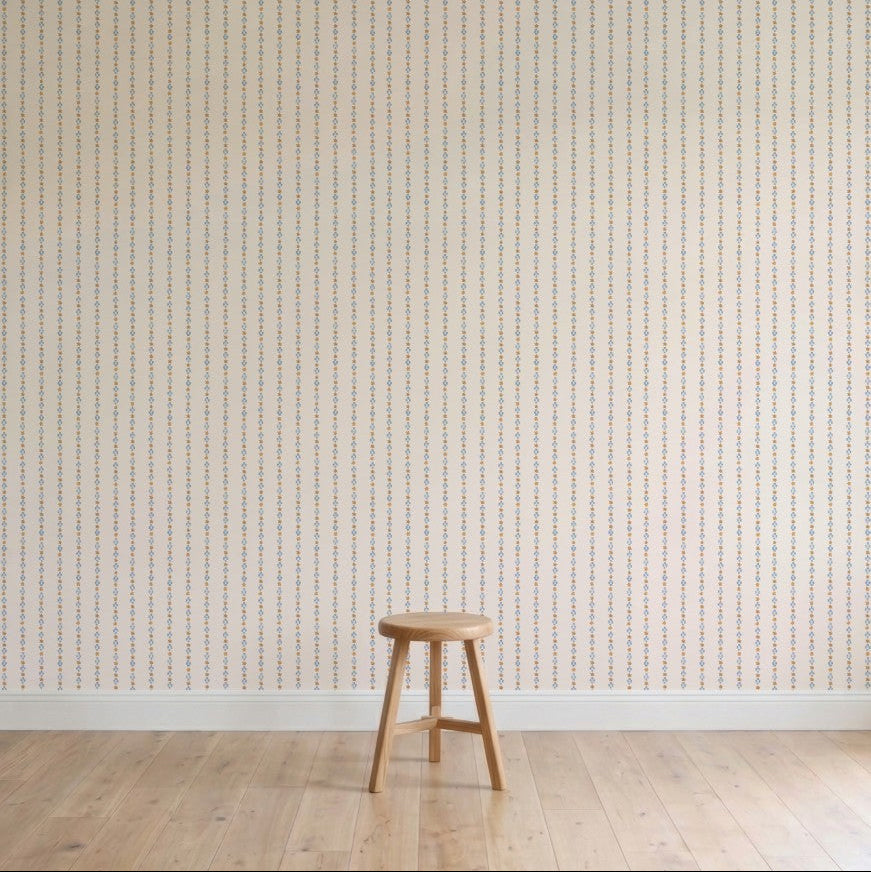 A simple wooden stool stands on a light wood floor against a plain wall with Jacquard Stars Wallpaper in gold, adding subtle elegance to the setting.