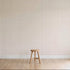 A simple wooden stool stands on a light wood floor against a wall decorated with Jacquard Stars Wallpaper, Red. The scene remains minimalistic and uncluttered.
